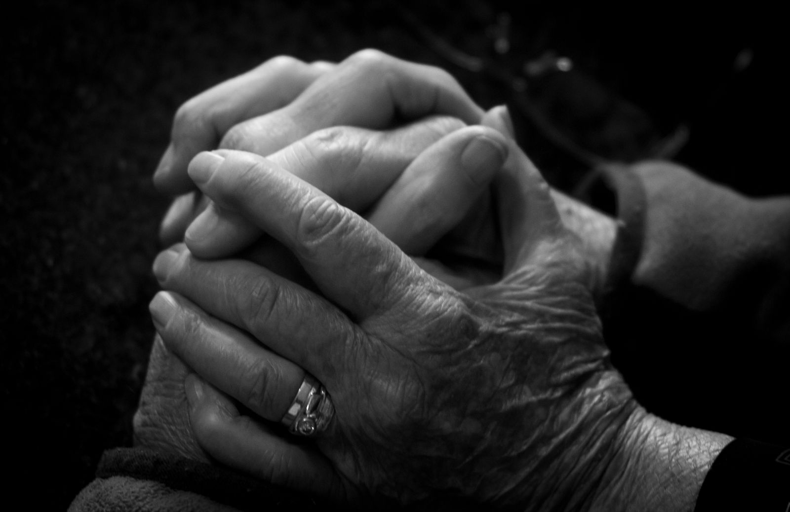 Adult daughter holding hands with her elderly mother on the couch